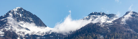 The mountains are covered in snow and the sky is clear. The clouds are white and fluffy, creating a peaceful and serene atmosphereの写真素材