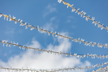 The sky is blue and clear with a few clouds. The wires are covered in ice and snowの写真素材