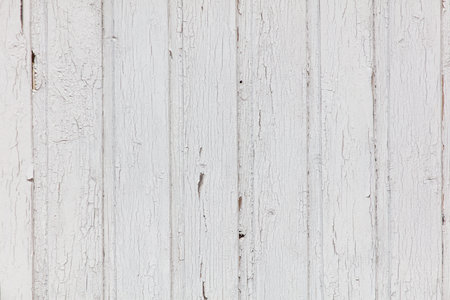 A white wooden wall with a lot of cracks and holes. The wall appears to be old and worn, giving it a rustic and weathered look. The cracks and holes in the wall create a sense of depth and textureの写真素材