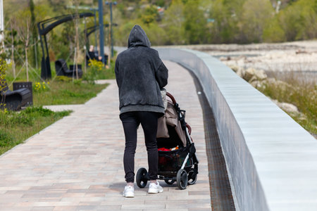 A man pushing a stroller on a sidewalk. The man is wearing a hoodie and he is walking on a pathの写真素材
