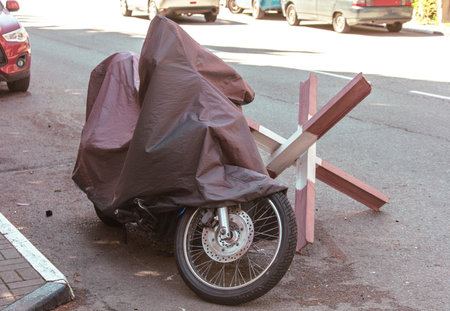 A motorcycle is covered in a black plastic tarp. The motorcycle is laying on the ground next to a wooden postの写真素材
