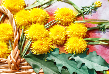 A beautiful embroidered piece of art features a basket filled with yellow flowers. The basket is made of brown material and is placed on a red backgroundの写真素材
