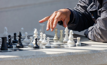 A man is playing chess with a white and black set of pieces. He is pointing at a piece on the boardの写真素材