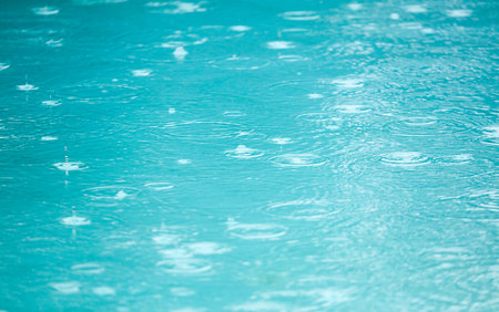 The water is blue and has raindrops on it. The raindrops are small and scattered throughout the waterの写真素材