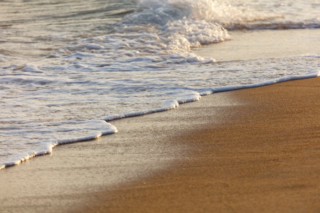 The ocean waves are crashing onto the shore, creating a beautiful and calming scene. The water is white and the sand is brown, giving the image a serene and peaceful atmosphereの写真素材