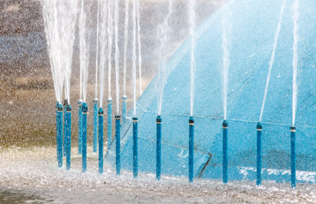 A blue water fountain with many blue water spouts shooting out of it. The water is spraying in all directionsの写真素材