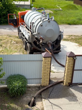 A large truck is dumping waste into a hole in the ground. The truck is parked next to a brick wallの写真素材