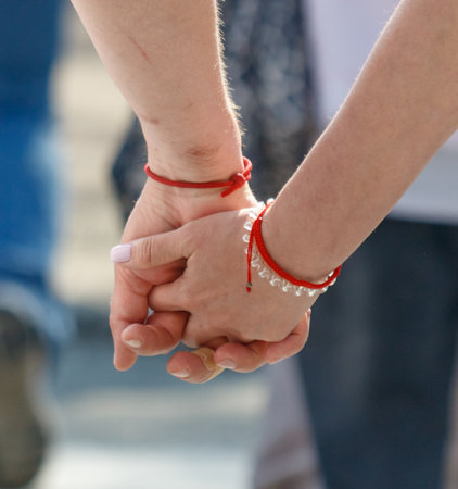 A man and a woman are holding hands, with each of them wearing a red bracelet. The bracelets are clear and shiny, adding a touch of elegance to their appearanceの写真素材