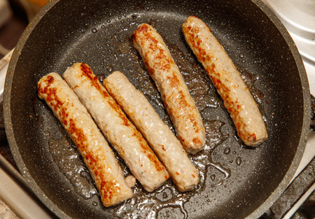 A pan of sausages is cooking on a stove. The sausages are browned and appear to be well-cookedの写真素材
