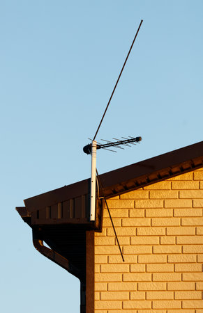 A black antenna is on the roof of a house. The sky is blue and the sun is shiningの写真素材