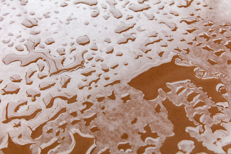 A brown surface with water droplets scattered all over it. The droplets are of various sizes and are spread out in different directionsの写真素材
