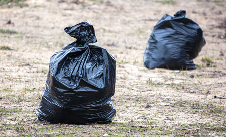 Two black plastic bags are on the ground. One is on the left and the other is on the rightの写真素材