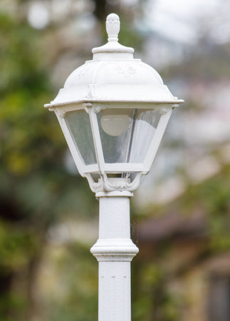 A white street light with a bulb in it is lit up. The light is shining brightly, illuminating the area around it. The light is positioned on a pole, which is standing upright in the groundの写真素材