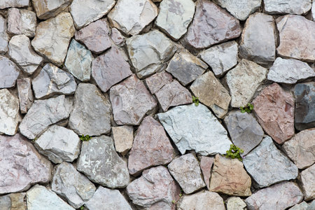 A wall made of gray and white stones. The wall is made of many different sized stones. The wall is...