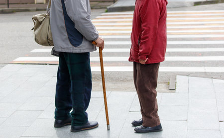 Two elderly people are standing on a sidewalk, one of them holding a cane. The scene is quiet and peaceful, with the two men looking at each otherの写真素材