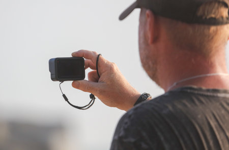 A man is holding a camera with a strap around his wrist. He is looking at the camera, possibly taking a pictureの写真素材