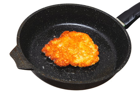 A piece of fried chicken is cooking in a pan. The pan is black and the chicken is golden brown