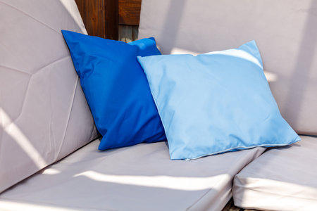 Two pillows, one blue and one white, are on a couch. The blue pillow is on the left and the white one is on the rightの写真素材
