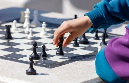 A child is playing a game of chess with a black and white board. The child is reaching for a piece, and the board is set up with a king and a queenの写真素材