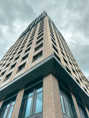 A tall building with a corner window. The building is brown and has a gray roof. The sky is cloudy...