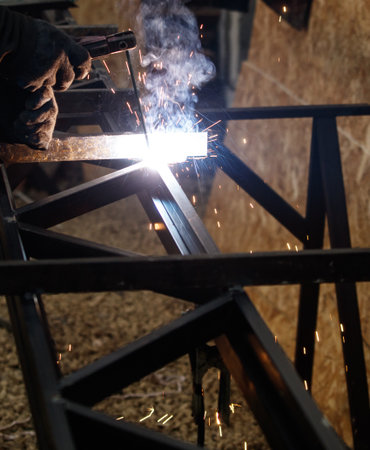 A man is welding metal in a workshop. The sparks from the welding process are flying everywhere,...