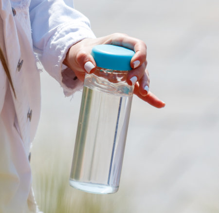 A person is holding a clear bottle with a blue lid. The bottle is filled with water. The person is...