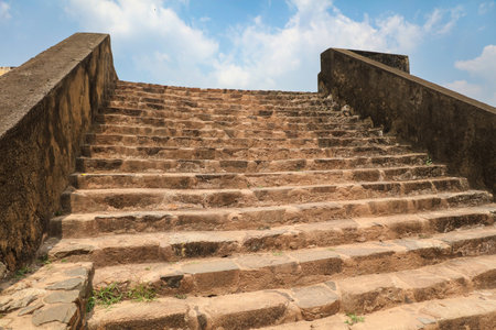 A stone staircase with a cloudy sky in the background. The steps are worn and the stone is roughの写真素材