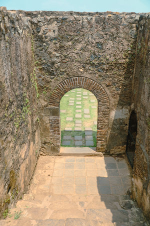 A small archway in a stone building with a brick floor. The archway is open and the floor is covered...