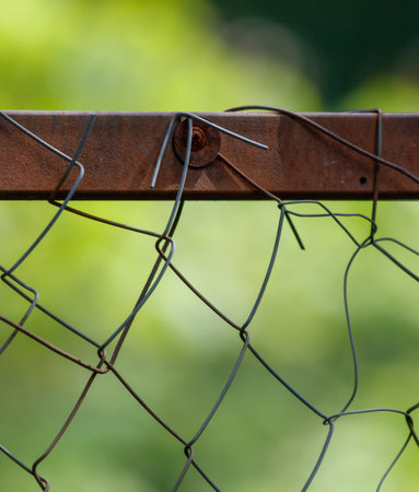 A rusty chain link fence with a green background. The fence is old and has a lot of rust on itの写真素材