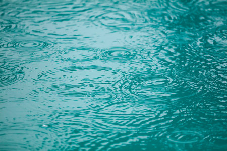 A body of water with raindrops falling on it. The water appears to be calm and still, with the...
