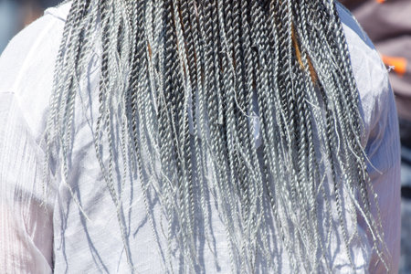 A woman with long, gray hair is wearing a white shirt. The hair is braided and has a silver and gray...