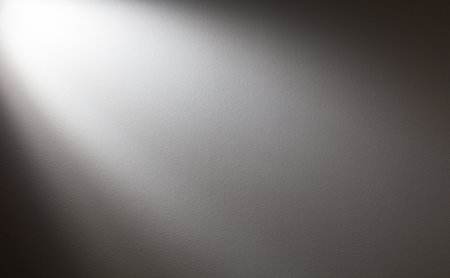 A gray background with a white light shining on it. The light is creating a shadow on the wallの写真素材
