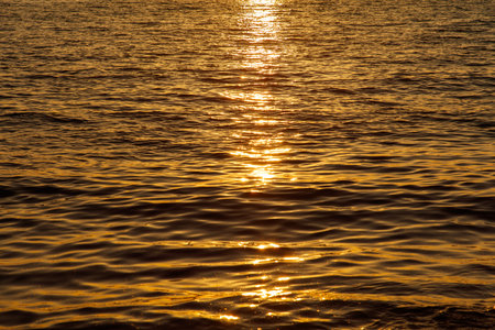 The water is calm and the sun is setting, creating a beautiful and serene atmosphere. The water is a deep blue color, and the sun's reflection is visible on the surfaceの写真素材
