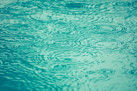 A body of water with raindrops falling on it. The water is a deep blue color, and the raindrops are...