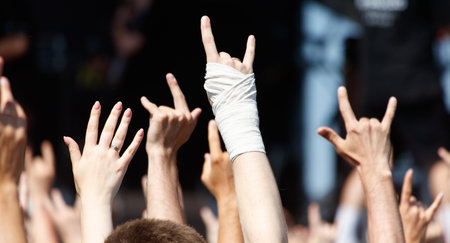 A crowd of people are holding up their hands and fingers in the air, with one person's hand having a...