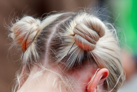A girl with her hair in a bun. The bun is on the top of her head. The bun is not very tight