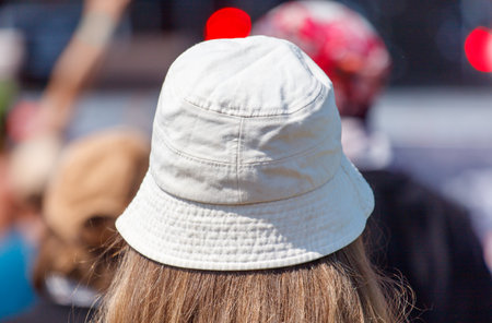 A woman wearing a white hat is standing in front of a crowd. The hat is tilted to the side, and the...