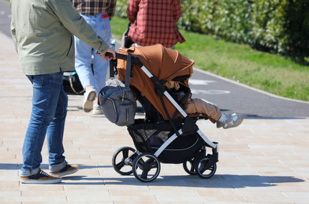 A man is pushing a stroller with a child in it. The stroller has a bag on it
