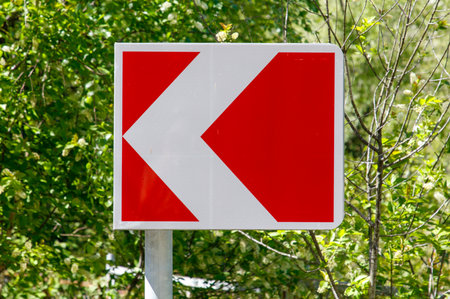 A red and white sign with a white arrow pointing to the right. The sign is in a forest with trees in...