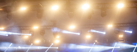 A stage with lights shining on it. The lights are yellow and white. The stage is lit up and it looks...