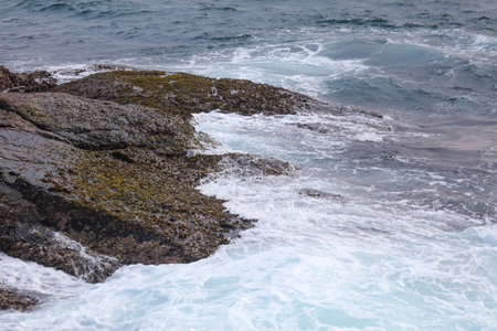 The ocean is rough and the rocks are covered in moss. The water is white and the waves are crashing...