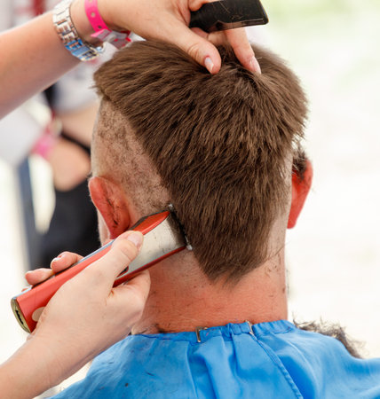 A man with a shaved head is getting his hair cut by a woman. The woman is using a pair of scissors and a razor to cut the man's hairの写真素材