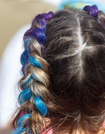 A girl with blue, purple, and brown hair is wearing a pink shirt. Her hair is braided and has a blue...