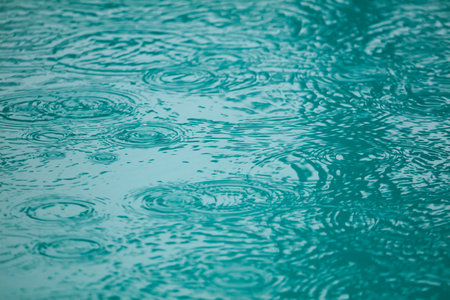 A body of water with raindrops falling on it. The water appears to be calm and still, with the...