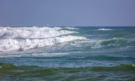 The ocean is calm and the waves are small. The sky is clear and blue. The water is a beautiful shade...
