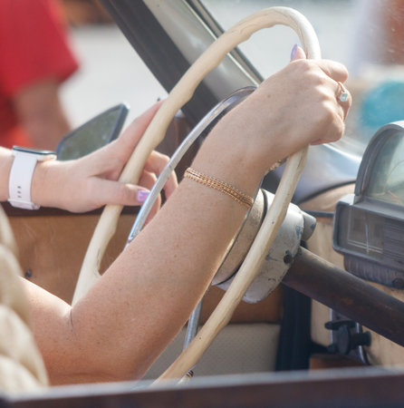 Woman is driving a car and is holding a cell phone in her hand. She is also wearing a bracelet