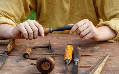 Man is sitting at a wooden table with a collection of tools, including a pair of pliers. The table...