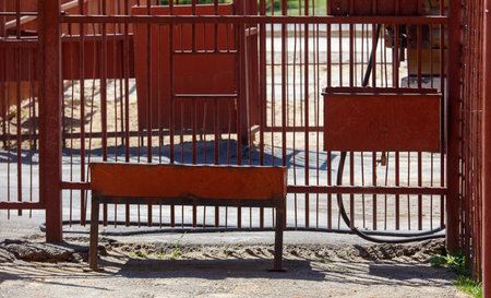 Bench is sitting in front of a fence. The bench is empty. There is a red container on the ground...