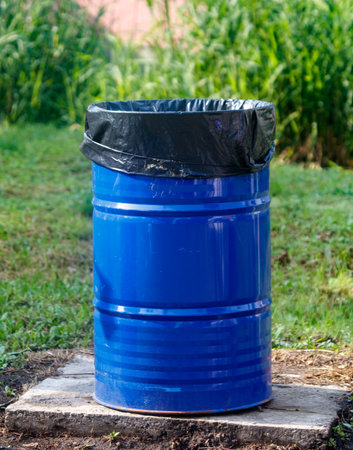 Blue trash can with a black plastic bag on top. The trash can is in a grassy areaの写真素材