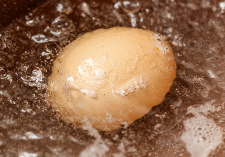 Fried egg is in a pan of water. The water is bubbling and the egg is cooking
